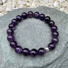 Load image into Gallery viewer, A handmade 10mm amethyst beaded stretch bracelet outside on a stone
