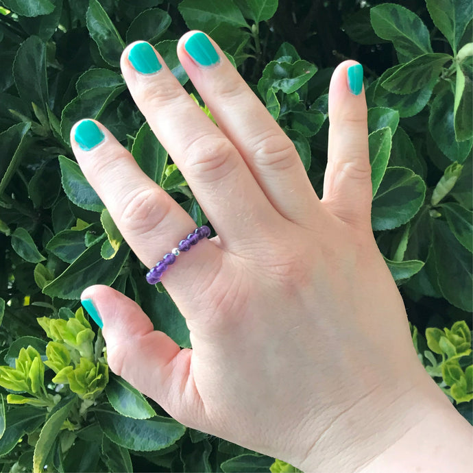 A hand wearing a beaded amethyst stretch ring.
