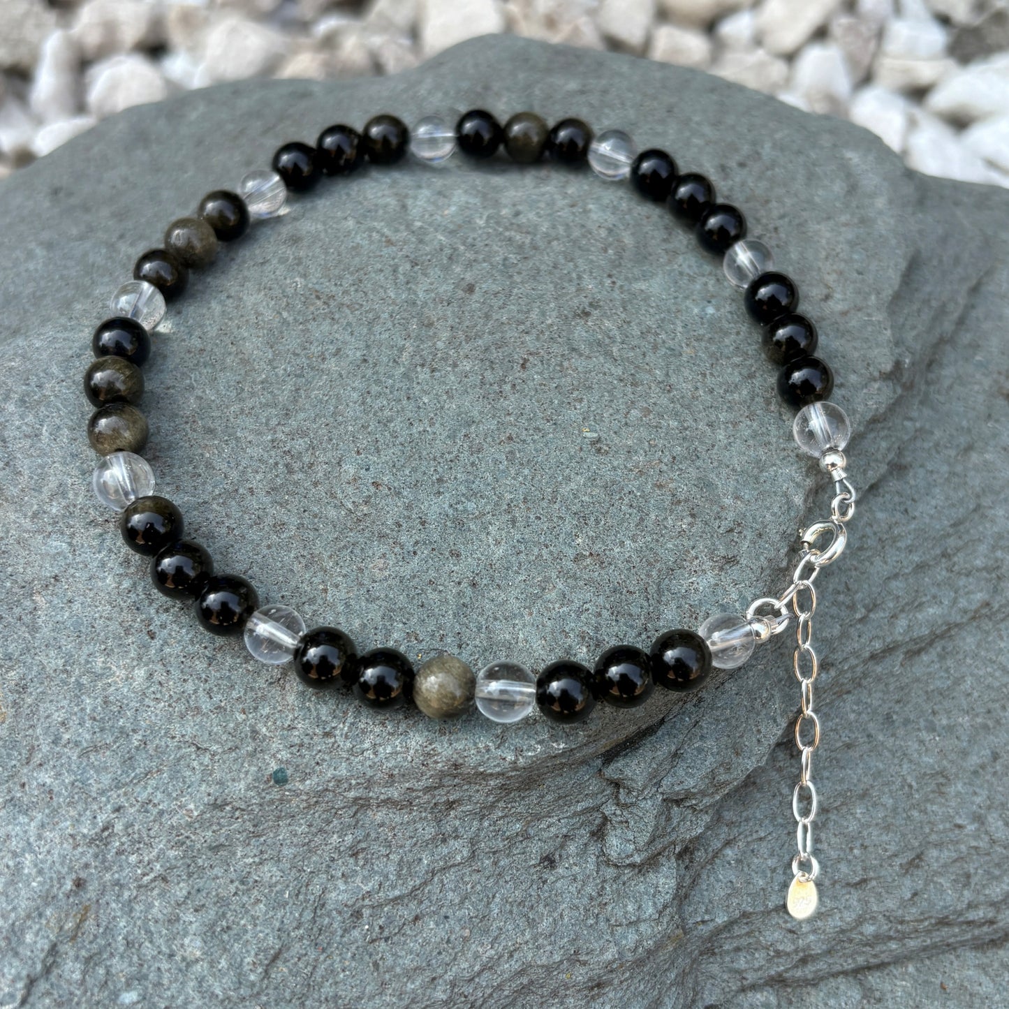 Beaded bracelet with black, clear, and brown beads on a stone surface