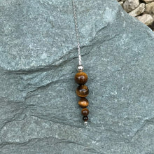 Load image into Gallery viewer, Tiger&#39;s eye crystal pendulum on stone
